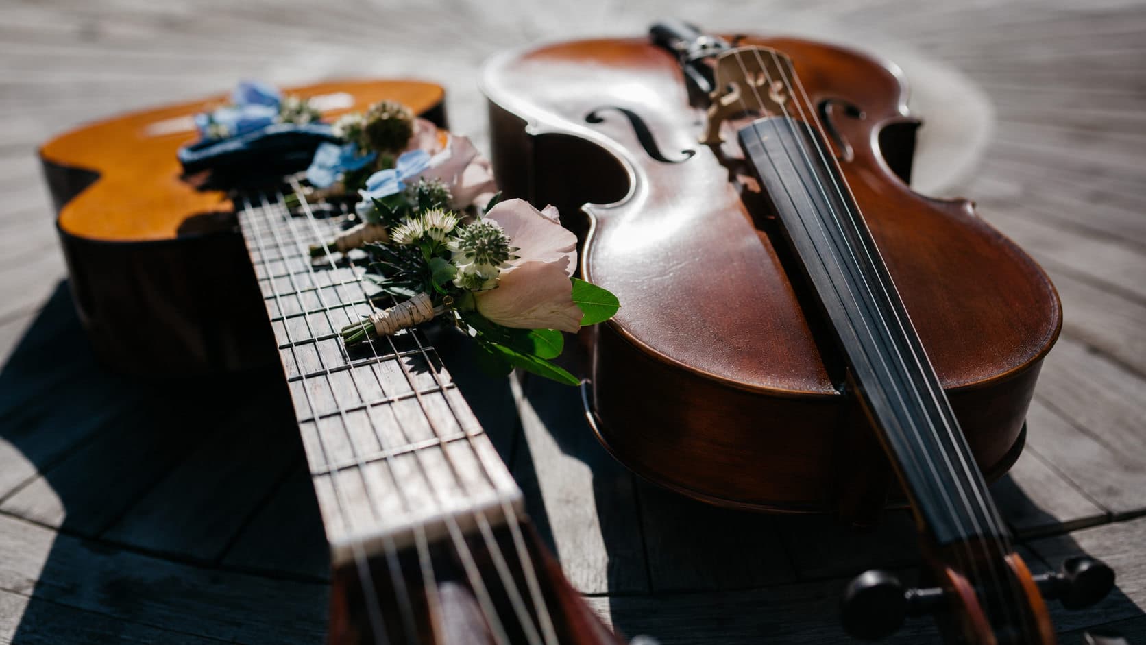 Acoustic guitar and violin decorated with flowers on a wooden floor